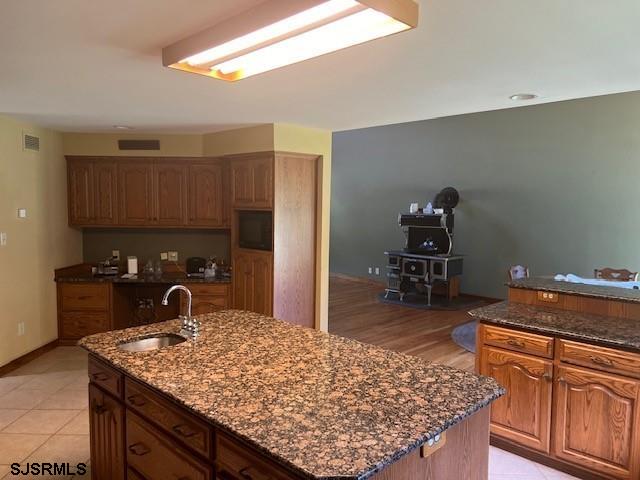 kitchen with a kitchen island with sink, visible vents, dark stone counters, and a sink