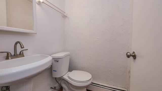 half bath featuring a sink, a baseboard heating unit, toilet, and a textured wall