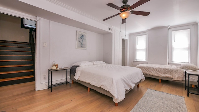 bedroom with ceiling fan, light wood-style flooring, visible vents, and ornamental molding