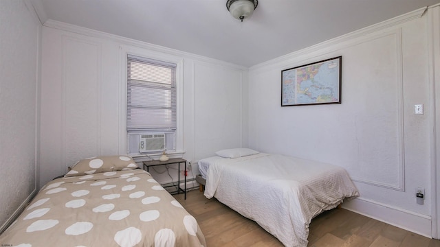 bedroom featuring cooling unit, baseboard heating, wood finished floors, and crown molding