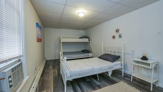 bedroom with baseboards, a paneled ceiling, wood finished floors, and a baseboard heating unit