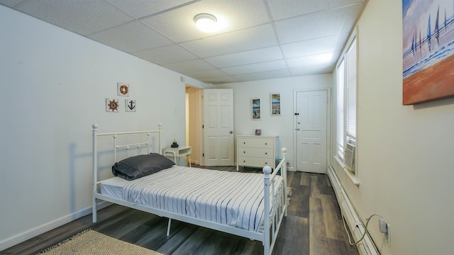 bedroom with a drop ceiling, baseboards, and dark wood-style flooring