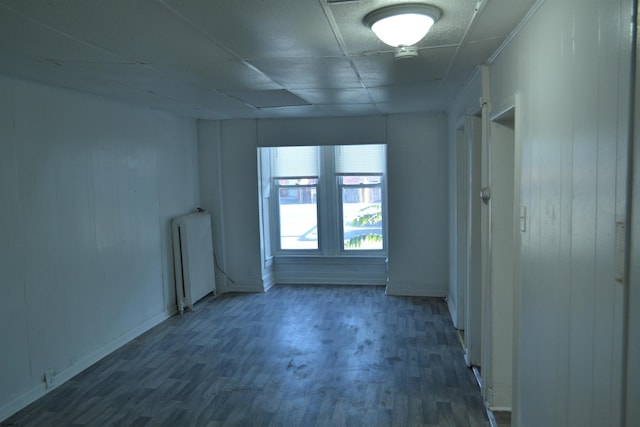 spare room with radiator heating unit, a drop ceiling, dark wood-type flooring, and wood walls