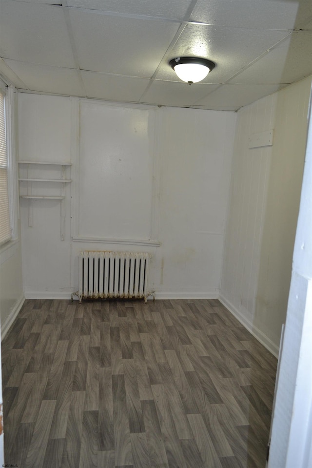 basement featuring radiator heating unit, a drop ceiling, and dark hardwood / wood-style floors