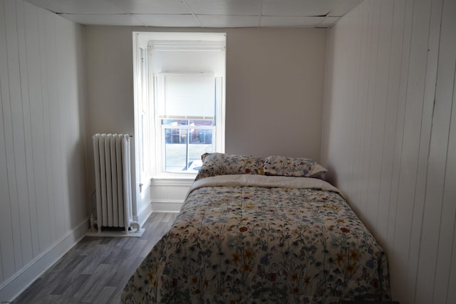 bedroom with a paneled ceiling, wooden walls, dark wood-type flooring, and radiator