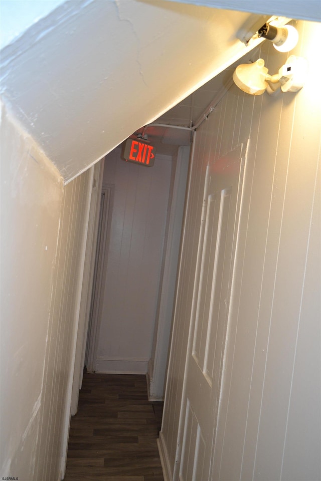 corridor featuring wood walls, dark wood-type flooring, and vaulted ceiling