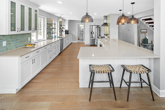 kitchen featuring light wood-style flooring, stainless steel appliances, a breakfast bar, decorative backsplash, and wall chimney exhaust hood