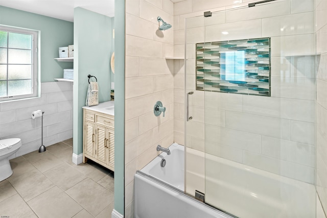 full bath featuring tile patterned flooring, toilet, shower / bath combination with glass door, vanity, and tile walls