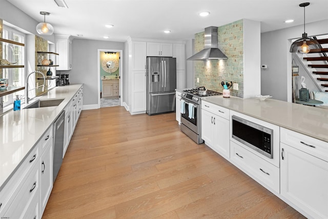 kitchen featuring tasteful backsplash, wall chimney exhaust hood, appliances with stainless steel finishes, light wood-style floors, and a sink