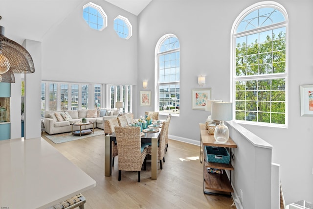 dining room featuring a towering ceiling, light wood-style flooring, and baseboards