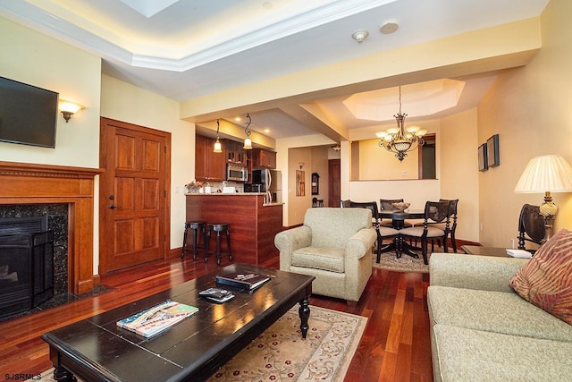 living room featuring dark wood-style floors, a tray ceiling, a notable chandelier, a premium fireplace, and baseboards