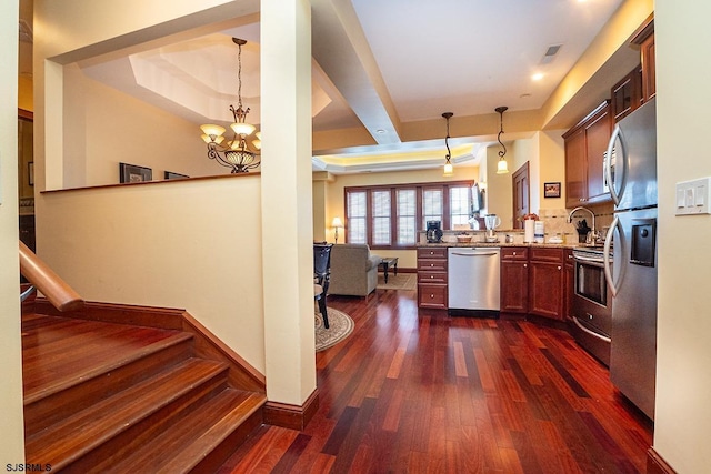 kitchen with dark wood-style flooring, pendant lighting, a raised ceiling, appliances with stainless steel finishes, and a peninsula