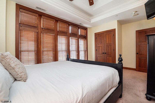 bedroom with a tray ceiling, light colored carpet, visible vents, ceiling fan, and baseboards