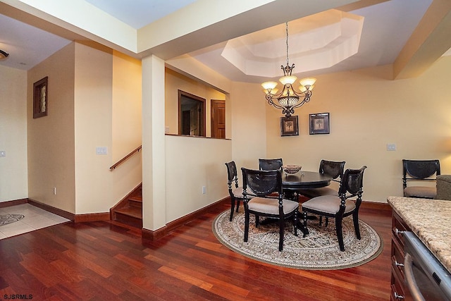 dining area featuring a chandelier, a raised ceiling, baseboards, and wood finished floors