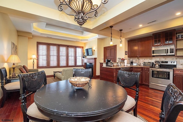 dining area with dark wood-style floors, a tray ceiling, visible vents, and a fireplace