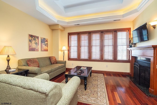 living room featuring baseboards, visible vents, a raised ceiling, a fireplace with flush hearth, and wood finished floors