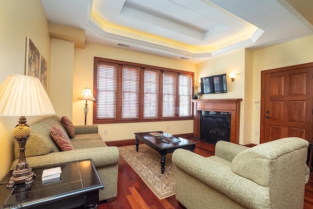 living area featuring a tray ceiling, visible vents, a fireplace, and wood finished floors