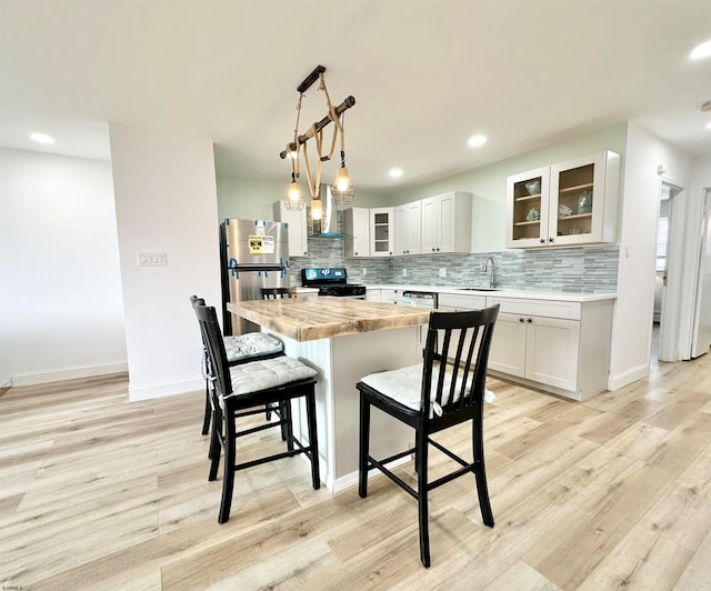 kitchen featuring light hardwood / wood-style floors, black range, wall chimney exhaust hood, white cabinets, and stainless steel fridge