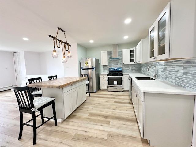 kitchen with light wood-type flooring, sink, stainless steel appliances, and wall chimney exhaust hood