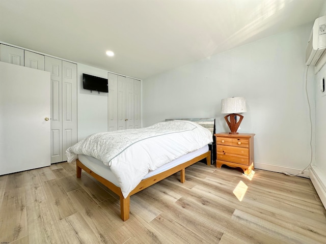 bedroom featuring light hardwood / wood-style flooring, a wall mounted AC, and two closets