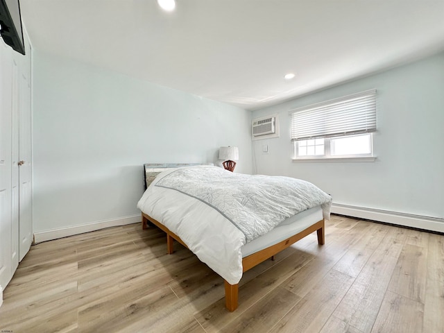 bedroom featuring light hardwood / wood-style floors, a baseboard heating unit, and a wall mounted air conditioner