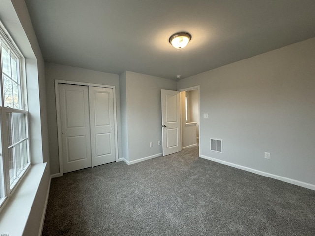 unfurnished bedroom with dark colored carpet, a closet, visible vents, and baseboards