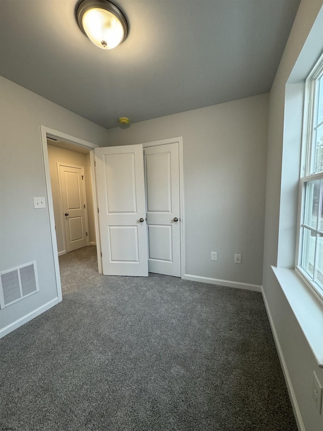 unfurnished bedroom with dark colored carpet, visible vents, and baseboards