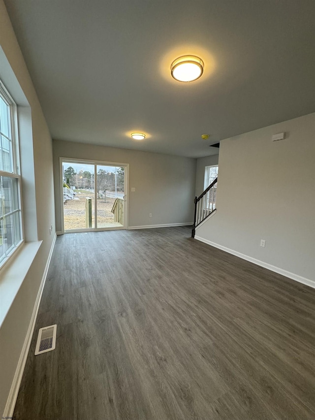 unfurnished living room featuring stairway, dark wood-style flooring, visible vents, and baseboards