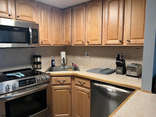 kitchen with tile counters, appliances with stainless steel finishes, sink, and decorative backsplash