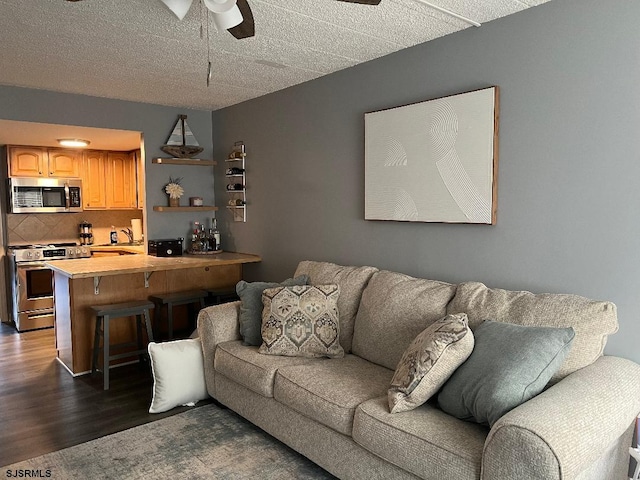 living room featuring ceiling fan, a textured ceiling, and dark wood-type flooring