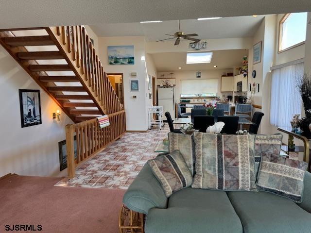 living area with stairs, ceiling fan, carpet floors, and a towering ceiling