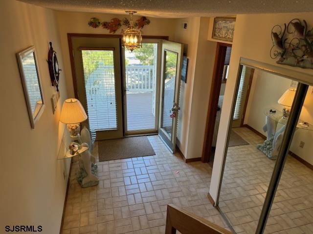 doorway to outside featuring baseboards, a notable chandelier, a textured ceiling, and brick patterned floor