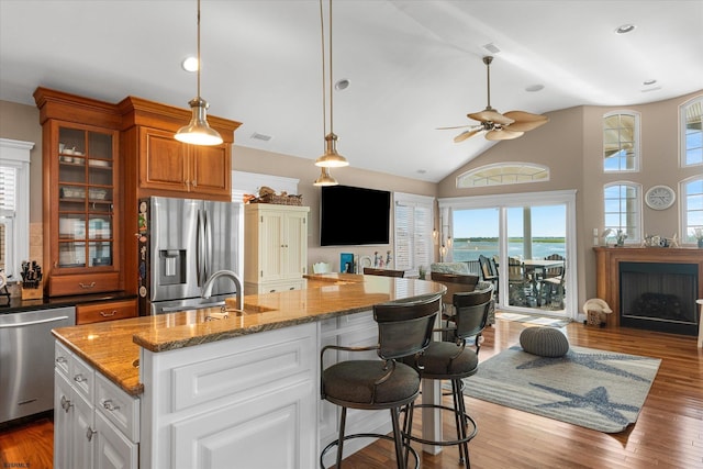 kitchen with stone countertops, wood finished floors, open floor plan, appliances with stainless steel finishes, and glass insert cabinets