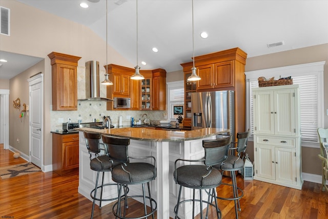 kitchen featuring stainless steel appliances, brown cabinetry, a sink, and wall chimney exhaust hood