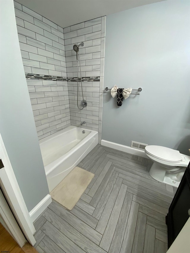 bathroom featuring parquet flooring, tiled shower / bath combo, and toilet