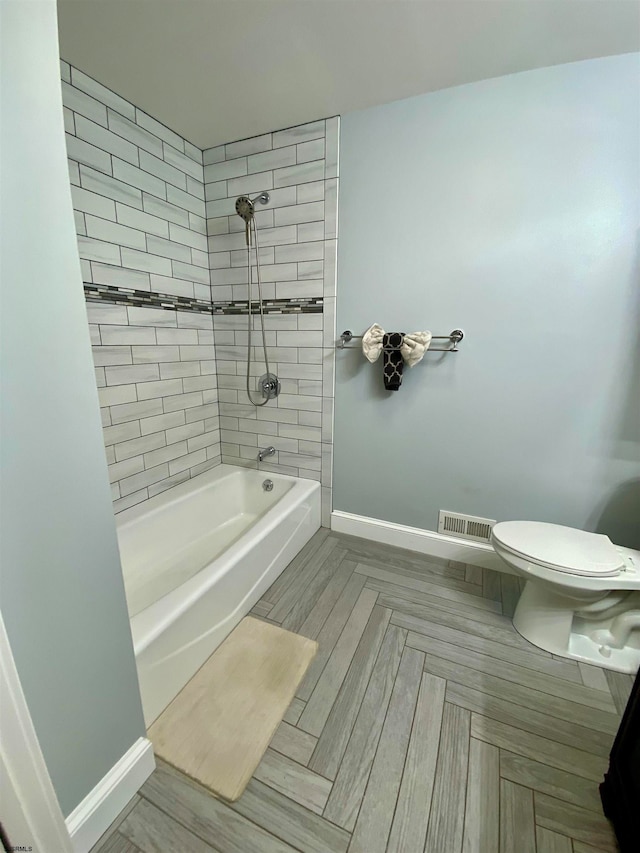 bathroom featuring toilet, parquet flooring, and tiled shower / bath combo