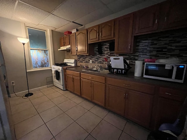 kitchen with white gas range oven, a drop ceiling, backsplash, light tile patterned floors, and sink