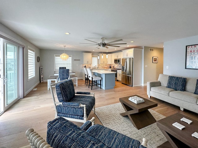 living room with a wealth of natural light, light hardwood / wood-style flooring, sink, and ceiling fan