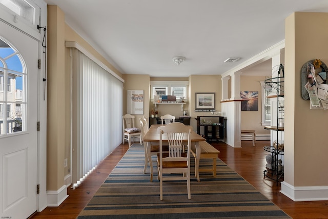 dining room featuring a baseboard heating unit, visible vents, baseboards, dark wood finished floors, and ornate columns