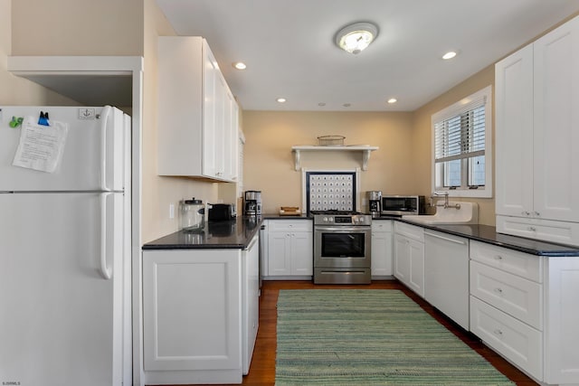 kitchen featuring stainless steel appliances, dark countertops, dark wood-type flooring, white cabinets, and a sink