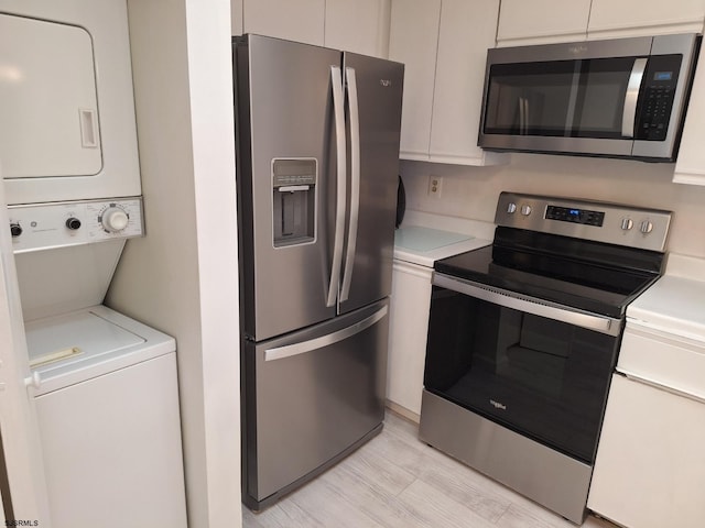 kitchen with stainless steel appliances, stacked washing maching and dryer, white cabinetry, and light hardwood / wood-style flooring