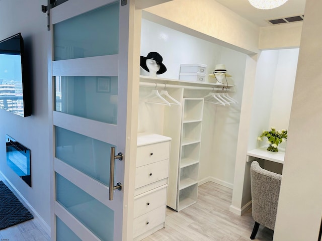 walk in closet with a barn door and light hardwood / wood-style floors