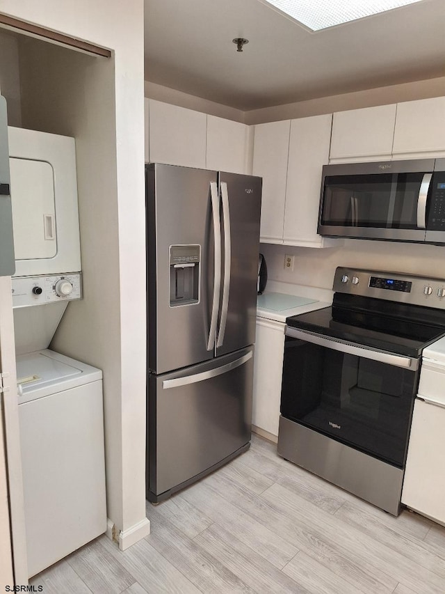 kitchen with stacked washing maching and dryer, light hardwood / wood-style flooring, appliances with stainless steel finishes, and white cabinets