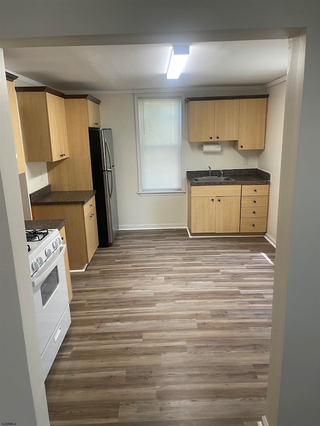 kitchen with stainless steel refrigerator, white range with gas stovetop, sink, hardwood / wood-style flooring, and light brown cabinets