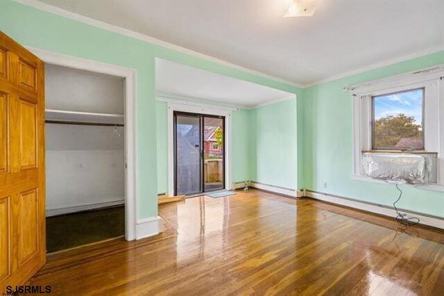 unfurnished bedroom featuring a closet, wood-type flooring, a baseboard radiator, and crown molding