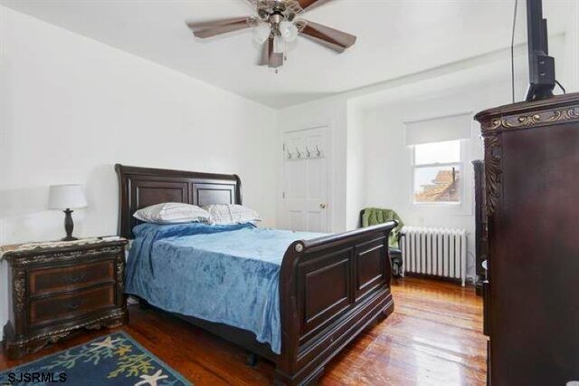 bedroom featuring dark wood-type flooring, ceiling fan, and radiator heating unit