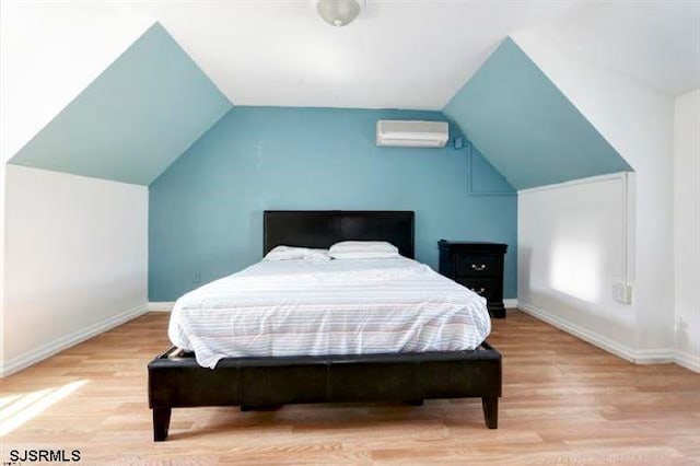 bedroom with light hardwood / wood-style floors, an AC wall unit, and vaulted ceiling