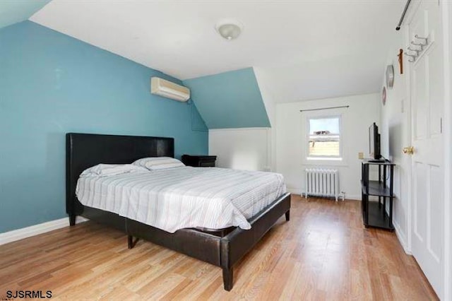 bedroom with radiator heating unit, vaulted ceiling, a wall unit AC, and light hardwood / wood-style floors