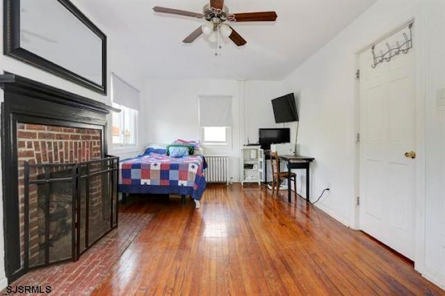 bedroom featuring ceiling fan, dark hardwood / wood-style floors, radiator heating unit, and a fireplace