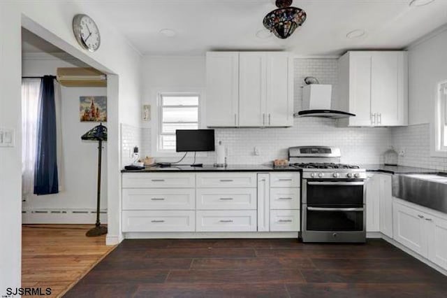 kitchen featuring wall chimney exhaust hood, stainless steel gas range, dark wood-type flooring, decorative backsplash, and a baseboard heating unit